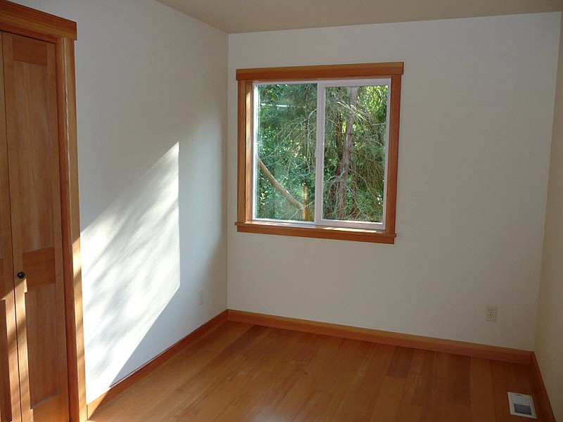 small upstairs bedroom with a wood trimmed window looking into the trees